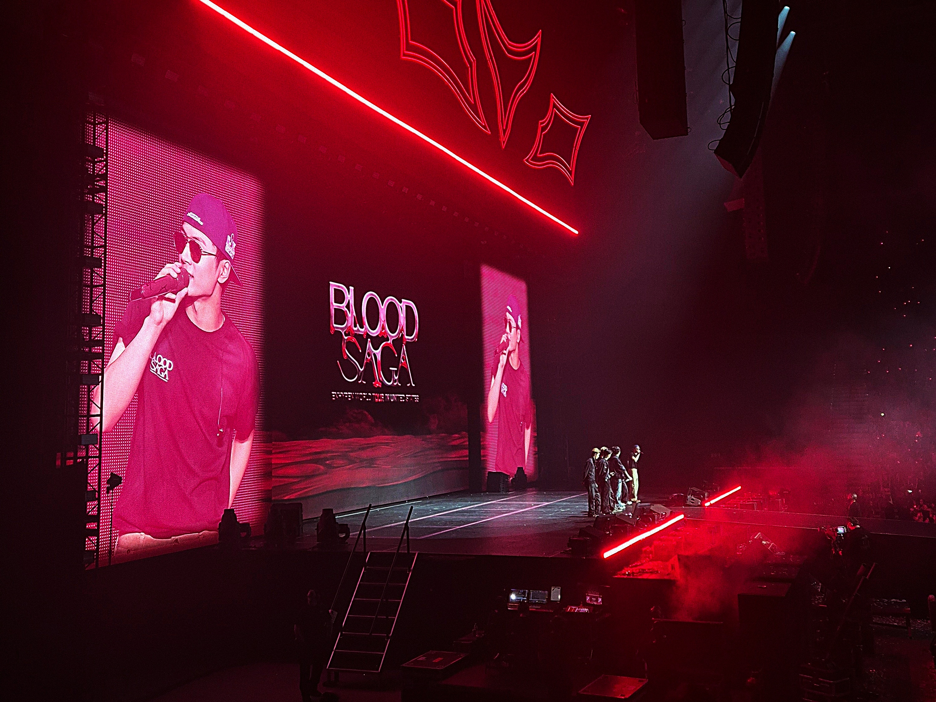 ENHYPEN’s ‘BLOOD SAGA’ World Tour stage at the Tacoma Dome in Tacoma, Washington, United States. On the large screens is the group’s oldest member, Jay, who is addressing the crowd. All six members stand on-stage toward the right of the image, with Jay at the farther end.